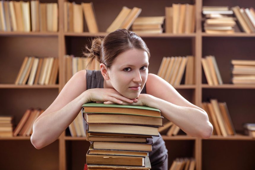 Młoda studentka oparła się o stos książek w bibliotece