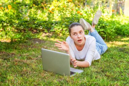 Koncepcja biznesowa freelancer. Młoda kobieta, leżąc na trawniku zielona trawa w parku miejskim pracy na komputerze typu laptop. Styl życia autentyczny szczery studentka studiująca na zewnątrz. Biuro mobilne