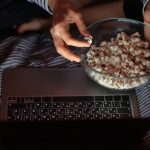 Kobieta w bluzie w paski i kapeluszu je popcorn i ogląda film w telewizji lub serialu o godz.