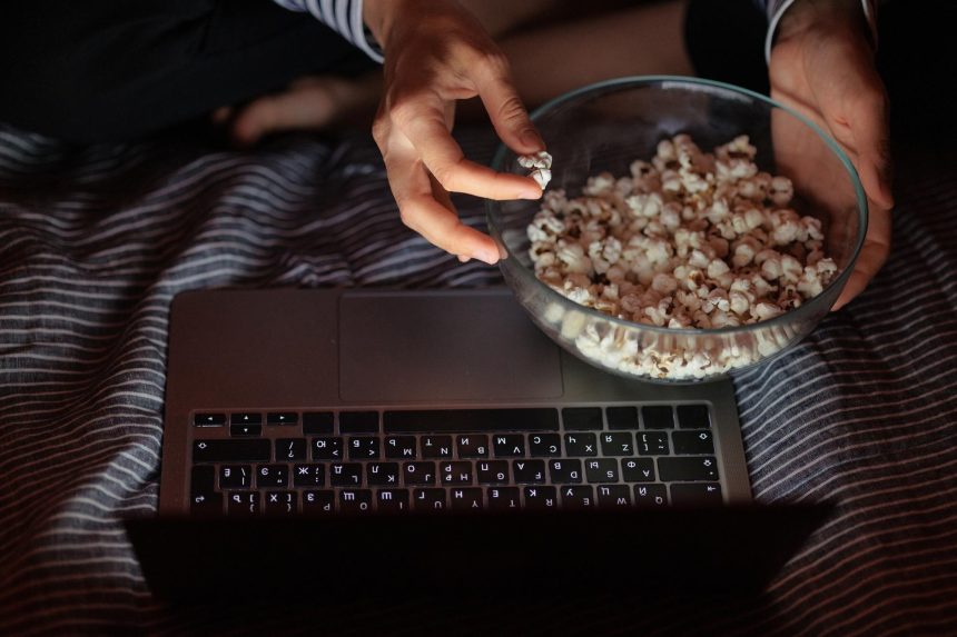 Kobieta w bluzie w paski i kapeluszu je popcorn i ogląda film w telewizji lub serialu o godz.