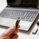 Kabel USB w dłoni zbliżenie Kamera akcji i laptop w tle Koncepcja przesyłania zdjęć i filmów