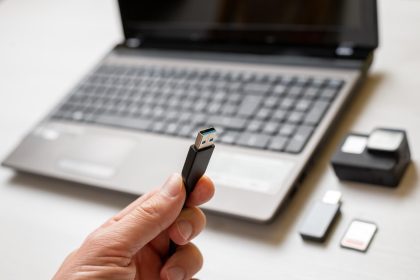 Kabel USB w dłoni zbliżenie Kamera akcji i laptop w tle Koncepcja przesyłania zdjęć i filmów