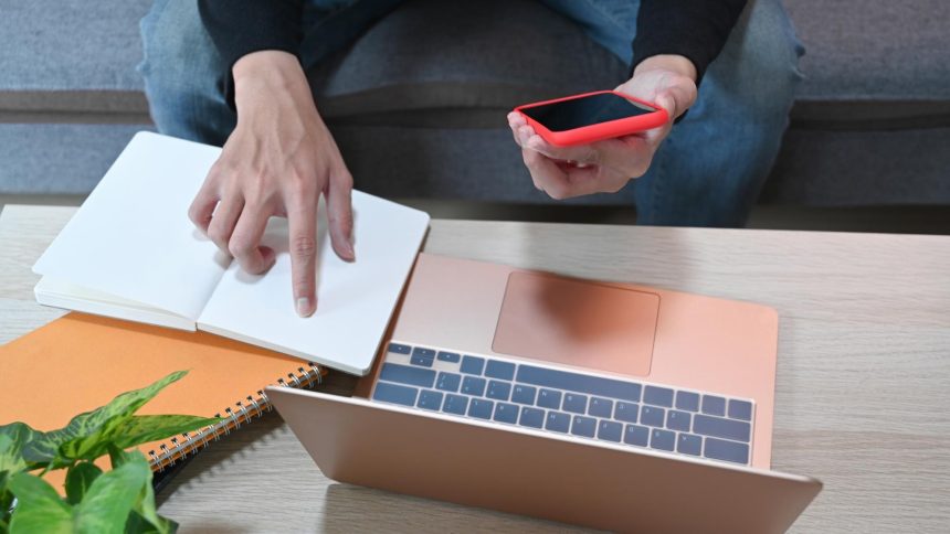 Mężczyzna trzymający smartfon i czytający informacje na notebooku