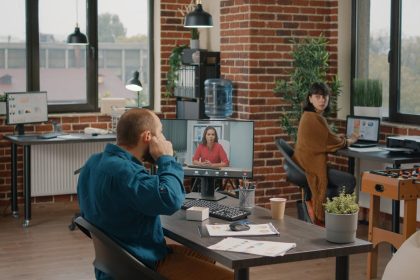Przedsiębiorca używający słuchawek dousznych, aby porozmawiać z menedżerem podczas rozmowy wideo w biurze startowym. Biznes człowiek rozmawia z kobietą na zdalnej wideokonferencji online na komputerze, aby zaplanować projekt i strategię.
