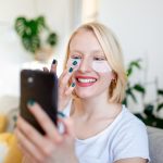 Piękna młoda uśmiechnięta brunetka z maską kosmetyczną Opaski na oczy i korzystająca z telefonu Atrakcyjna kobieta rozmawia przez telefon