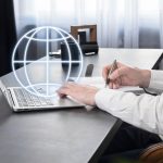 Biznesmen pracujący na laptopie wyszukujący informacje w Internecie robiący notatki w planerze analizującym rynek globalny lub komunikujący się z międzynarodowymi partnerami