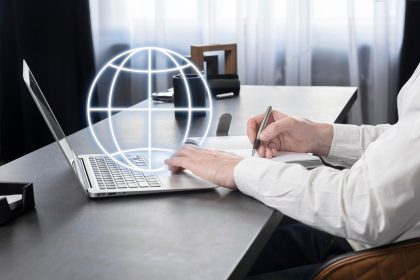 Biznesmen pracujący na laptopie wyszukujący informacje w Internecie robiący notatki w planerze analizującym rynek globalny lub komunikujący się z międzynarodowymi partnerami