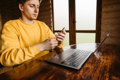 Facet pracuje w domku przy stole w pokoju z drewnianym wnętrzem używa smartfona