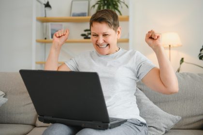 Podekscytowana dojrzała kobieta patrząca na ekran laptopa czytająca dobre wieści w wiadomości świętującej wygraną w loterii online cieszący się sukcesem zachwycona starsza kobieta siedząca na kanapie w domu przy komputerze