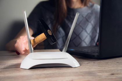 Ręka z młotkiem i routerem z modemem internetowym