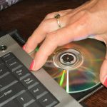 Ręka kobiety biorąca płytę DVD z laptopa