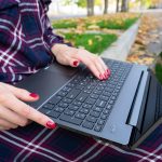 Student studiujący na zewnątrz Zbliżenie nowoczesnej dziewczyny siedzącej na trawie pod laptopem w parku Ręce na klawiaturze