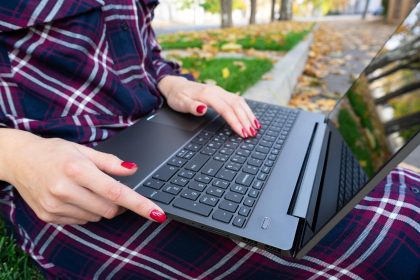 Student studiujący na zewnątrz Zbliżenie nowoczesnej dziewczyny siedzącej na trawie pod laptopem w parku Ręce na klawiaturze