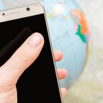 smartfon z czarnym ekranem w męskiej dłoni na tle mapy i kuli ziemskiej