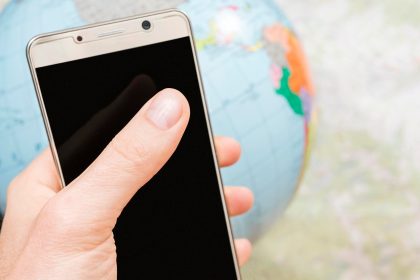 smartfon z czarnym ekranem w męskiej dłoni na tle mapy i kuli ziemskiej