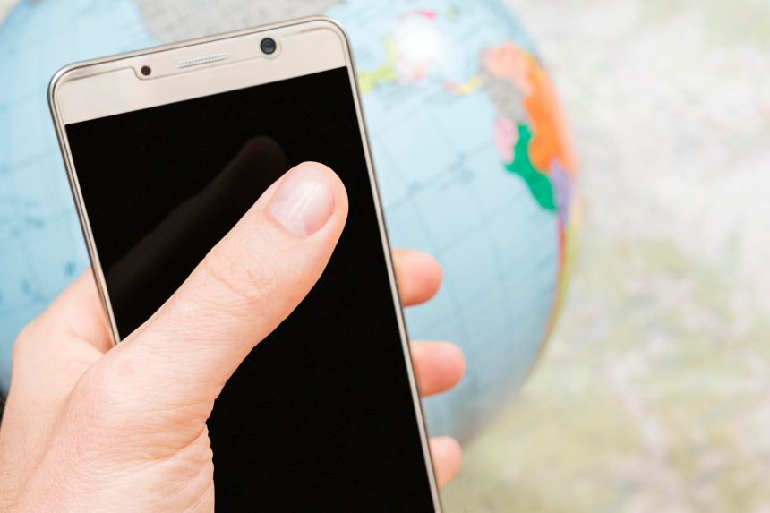smartfon z czarnym ekranem w męskiej dłoni na tle mapy i kuli ziemskiej