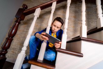 Chłopiec bawiący się smartfonem siedzący na schodach Widok od dołu