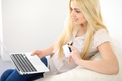 Szczęśliwa kobieta robi zakupy online w domu. Zbliżenie dłoni trzymającej kartę kredytową obok laptopa.
