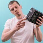 Mężczyzna pokazuje palcem wskazującym złącze zasilacza komputera na niebieskim tle Ręka Elektryczność Elektroniczne elementy zasilania Połączenie Sprzęt Jednostka Elektryczna