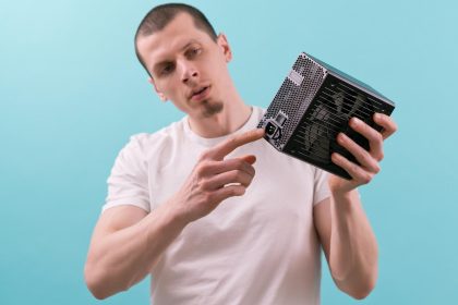 Mężczyzna pokazuje palcem wskazującym złącze zasilacza komputera na niebieskim tle Ręka Elektryczność Elektroniczne elementy zasilania Połączenie Sprzęt Jednostka Elektryczna