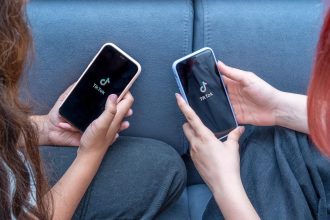 Dwie nastolatki z telefonami w rękach siedzą w domu na łóżku. Tiktok mediów społecznościowych jest ładowany na ekranie.