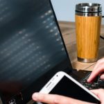 Kobieta korzystająca z telefonu komórkowego w biurze z laptopem i kawą