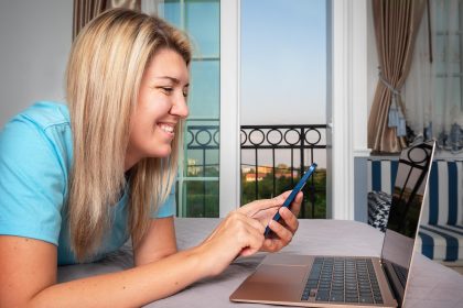 Dziewczyna leży na łóżku i pracuje z laptopem i telefonem