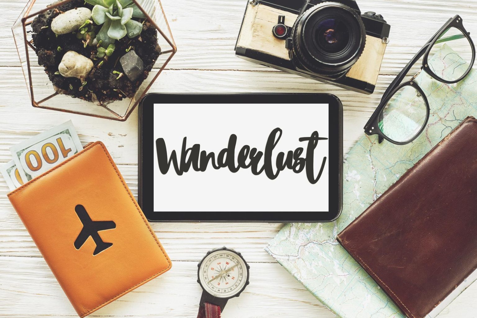 Wanderlust znak tekstowy na tablecie z pustym ekranem koncepcja podróży mapa pieniędzy kompas aparat okulary portfel na białym drewnianym tle widok z góry planowanie letnie wakacje wakacje eksploruj więcej