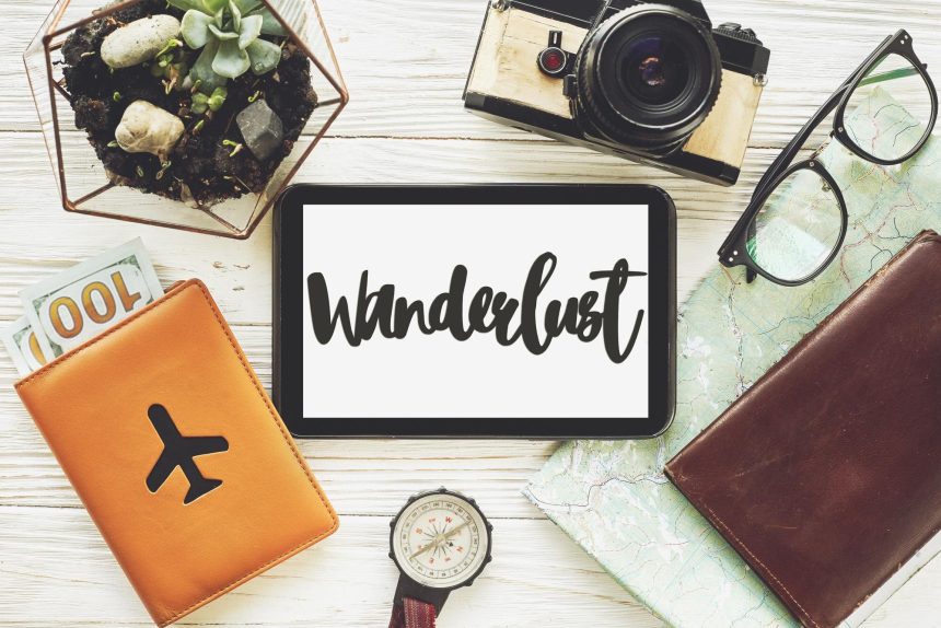 Wanderlust znak tekstowy na tablecie z pustym ekranem koncepcja podróży mapa pieniędzy kompas aparat okulary portfel na białym drewnianym tle widok z góry planowanie letnie wakacje wakacje eksploruj więcej