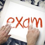 Ręką dotykającą słowa egzamin na pasku wyszukiwania na ekranie tabletu na zmiętych papierach
