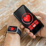 biznes, technologia, opieka zdrowotna i koncepcja ludzi - zbliżenie męskiej dłoni trzymającej smartfon i noszącej inteligentny zegarek z czerwoną ikoną bicia serca na ekranie