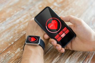 biznes, technologia, opieka zdrowotna i koncepcja ludzi - zbliżenie męskiej dłoni trzymającej smartfon i noszącej inteligentny zegarek z czerwoną ikoną bicia serca na ekranie