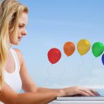 Ładna blondynka używa swojego laptopa na plaży przed kolorowymi balonami