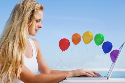 Ładna blondynka używa swojego laptopa na plaży przed kolorowymi balonami