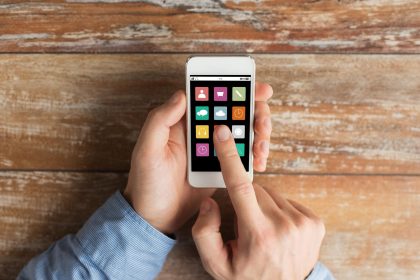 koncepcja biznesu, edukacji, ludzi i technologii - zbliżenie męskich rąk trzymających smartfon i wskazujących palcem na ikony aplikacji na ekranie