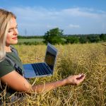 Kobieta rolnik sprawdzająca jakość rzepli stojąca na polu rzepli i trzymająca laptop