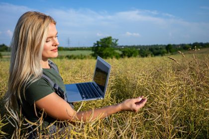 Kobieta rolnik sprawdzająca jakość rzepli stojąca na polu rzepli i trzymająca laptop