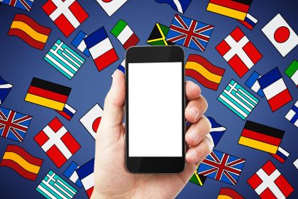 Zbliżenie męskiej ręki trzymającej pusty ekranowy smartfon z abstrakcyjnymi kolorowymi rysunkami flagi Aplikacja do tłumaczenia podróży i koncepcja nauki języka
