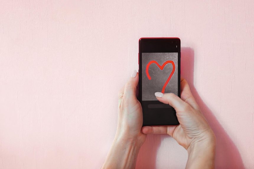 kobiece ręce trzymają telefon, w którym narysowane jest czerwone serce jako deklaracja miłości, miejsce na kopię