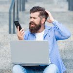 Brodaty mężczyzna czyta szokujące wiadomości na telefon komórkowy Zszokowany mężczyzna patrzy na telefon komórkowy