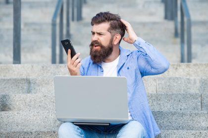 Brodaty mężczyzna czyta szokujące wiadomości na telefon komórkowy Zszokowany mężczyzna patrzy na telefon komórkowy