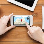 koncepcja technologii, biznesu, ludzi i nawigacji - zbliżenie kobiety z mapą nawigatora gps na ekranie smartfona i filiżanką kawy na drewnianym stole