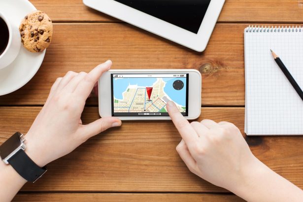 koncepcja technologii, biznesu, ludzi i nawigacji - zbliżenie kobiety z mapą nawigatora gps na ekranie smartfona i filiżanką kawy na drewnianym stole