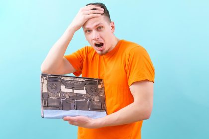 zszokowany mężczyzna trzymający głowę i otwarty brudny i zakurzony laptop na niebiesko. Przegrzanie