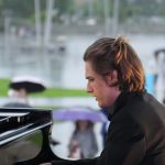 Utalentowany pianista występuje na wydarzeniu na świeżym powietrzu, podczas gdy odważni uczestnicy cieszą się deszczową pogodą.