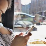 Profil młodej jasnowłosej kobiety korzystającej z telefonu komórkowego lub gadżetu mobilnego siedzącego w kawiarni