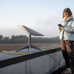 Kobieta z telefonem korzysta z internetu satelitarnego starlink na dachu