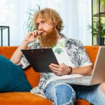 Młody freelancer pracuje z dokumentami z domu, analizuje informacje, przygotowuje raport finansowy.