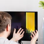Frustrated person with hands reacting to a severely broken computer monitor displaying colorful lines signifying technical damage repair and unexpected expense
