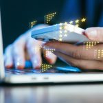 Person using a smartphone while typing on a laptop with digital feedback icons above